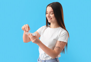 Young woman with container of vitamin supplements on blue background