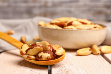 Spoon with tasty Brazil nuts on light wooden table, closeup