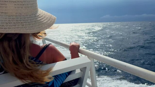 Anonymous blonde lady wearing straw hat on a cruise around tropical islands in the ocean. Female person on sea journey. Voyage for adult woman. Film grain pixel texture. Live camera. Soft focus.
