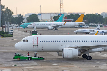 View of the airport platform, the plane rolls out the tow tractor push back before starting the engine and departure for the flight. In the distance, many other airliners near the terminal.