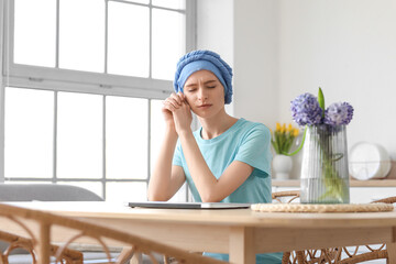 Fototapeta na wymiar Tired teenage girl after chemotherapy sitting at table in kitchen