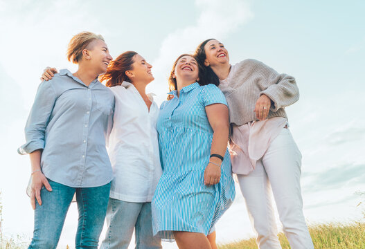 Portrait of four cheerful smiling and laughing women embracing during sunset time outdoors walking by the green hill. Woman's friendship, relations, and happiness concept image.