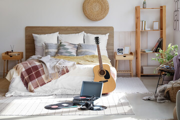 Record player with vinyl disks and guitar in interior of bedroom