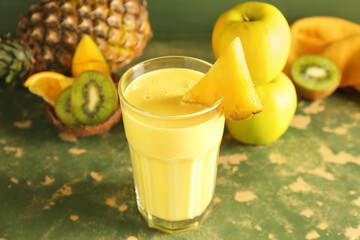Glass of tasty pineapple smoothie, kiwi and apple on green grunge table
