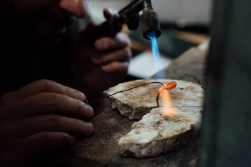 Close up of Jeweler crafting golden bracelet with flame torch.