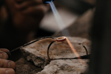 Close up of Jeweler crafting golden bracelet with flame torch.