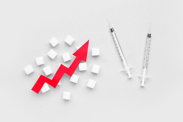 Sugar cubes with syringes for insulin injection and arrow directed upwards on white background