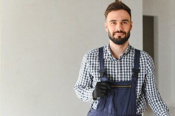Portrait of handsome mechanic with stubble in blue overall, shirt having his arms crossed, looking...