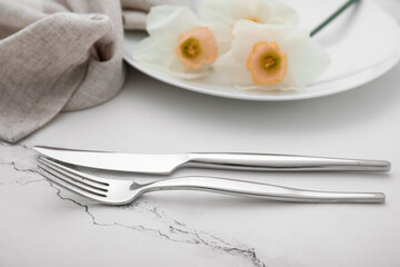 Fork, knife and plate with beautiful narcissus flowers on white marble table