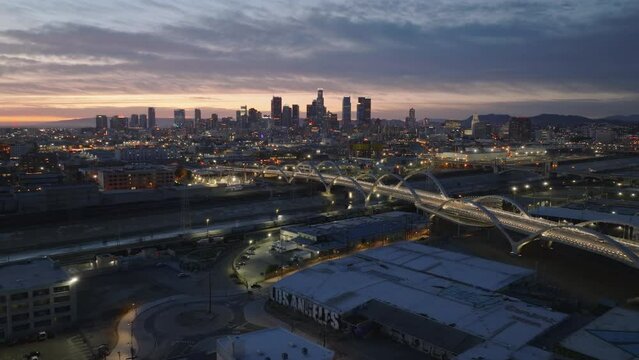 Aerial panoramic view of metropolis at dusk. Illuminated 6th Street Viaduct and downtown skyscrapers against colourful sky. Los Angeles, California, USA