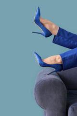 Female legs in high heels on sofa against blue background