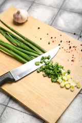 Wooden board with fresh cut green onion on dark tile background