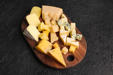 Wooden board with pieces of tasty cheese on dark background