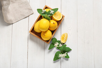 Wooden box of lemons with blooming branches on white table