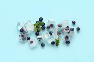 Ripe blueberry frozen in ice cubes and fresh berries on blue background