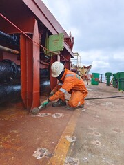 A ship crew or seaman is chipping or derusting main deck onboard a cargo ship or bulk carrier during maintenance period