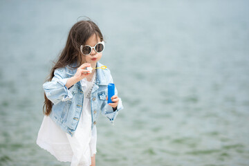 Cute little girl blowing soap bubbles on the beach. Active caucasian small daughter kid child spending time outdoors along river lake sea