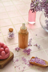 Obraz na płótnie Canvas Bottles of cosmetic oil with beautiful lilac flowers and sea salt on pink tile table