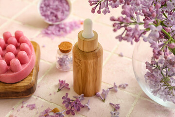 Fototapeta na wymiar Bottles of cosmetic oil with beautiful lilac flowers and sea salt on pink tile table