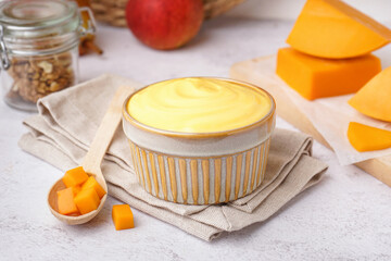 Bowl of tasty cheddar sauce and spoon with cheese cubes on white grunge background