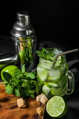 Mason jar of cold mojito and ingredients on dark background