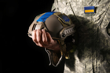 Ukrainian soldier with helmet on dark background, closeup