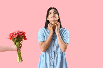 Allergic young woman scratching herself and female hand with tulips on pink background