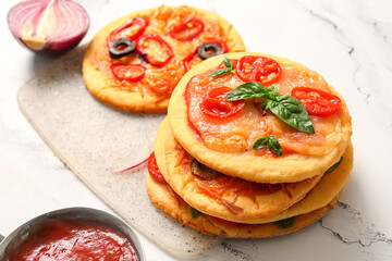 Board with different tasty mini pizzas on white background
