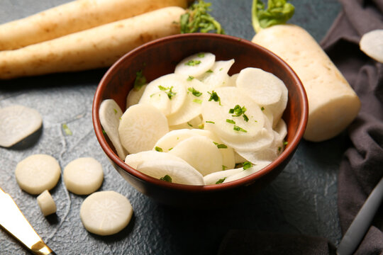 Bowl with slices of fresh daikon radish on dark background