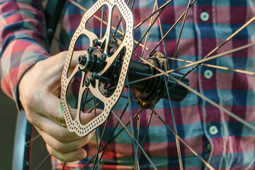Brake disc on a bicycle wheel close-up. A bicycle mechanic in a fashionable plaid shirt holds a wheel in his hands. Bicycle repair in the workshop on a black background. Details of a mountain bike.