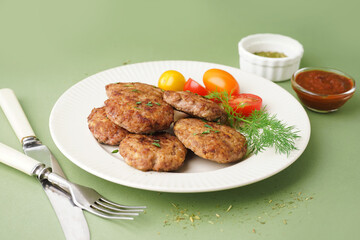 Plate with cutlets, dill and tomatoes on green table in kitchen