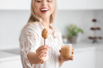 Young woman with spoon of nut butter in kitchen, closeup