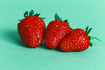 Three strawberries on a cyan background. for design with space for text. Header for design. Red ripe strawberry with leaves