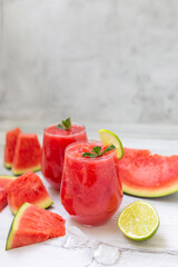 Watermelon smoothies with slices of fruit and leaf of mint and lime over white wooden background.