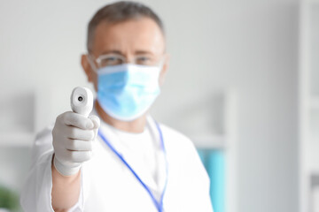 Mature male doctor with infrared thermometer in clinic, closeup