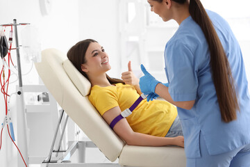 Female nurse preparing young donor for blood transfusion in clinic