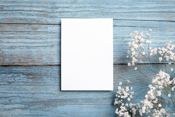 Card mockup, white blank wedding invitation with floral decor on bue wooden background. Greeting...