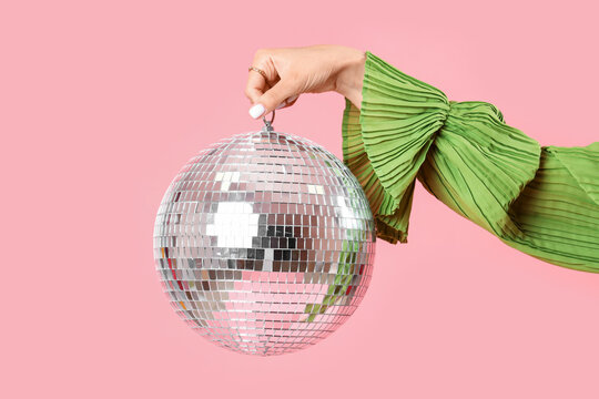 Fashionable woman in stylish green dress holding disco ball on pink background