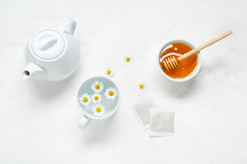 Fototapeta na wymiar Composition with teapot, cup of water, chamomile flowers, honey and tea bags on light background