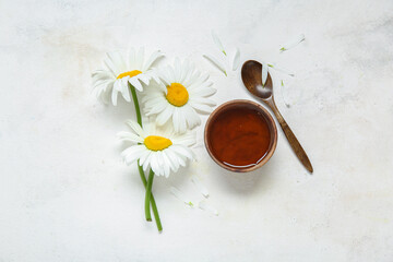 Obraz na płótnie Canvas Bowl of honey, spoon and beautiful chamomile flowers on light background