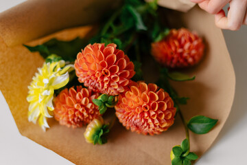 Horizontal image of orange dahlias wrapped in kraft paper lying on the table. Concept of autumn flowers, ideas for a gift