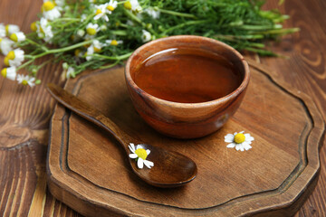 Board with bowl of honey and fresh chamomile flowers on wooden background, closeup