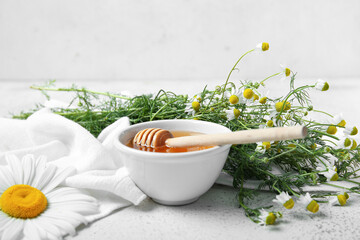 Bowl of honey and fresh chamomile flowers on light background