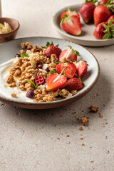 Healthy breakfast: fresh granola, muesli with yogurt, strawberry and honey on beige textured background. Copy space