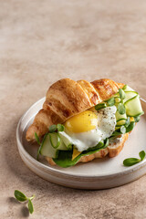 Delisious breakfast with croissant sandwich with fried egg, cheese, cucumber and micro greens and coffee over beige background close up with text space