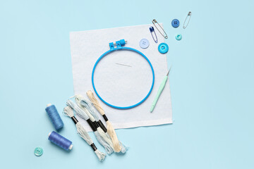 Plastic embroidery hoop with canvas and sewing supplies on blue background