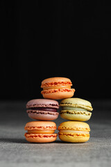 Colorful macaroons stacked in a pile on a grey table, black background