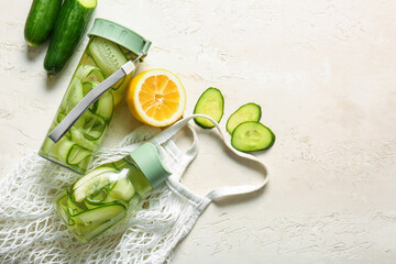 Sports bottles of infused water with cucumber slices and string bag on white background