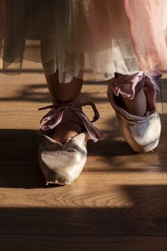 Little girl with a pink dress trying to do the first ballet step with her mother toe shoes