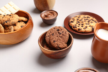 Bowls with cookies, chocolate and jug of milk on white background